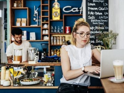 Young woman works at a laptop while sitting in a café.