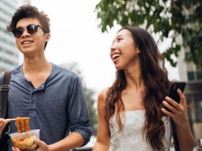 A smiling couple chats while walking down an urban sidewalk.