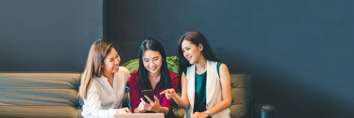 Three women look at a smartphone.