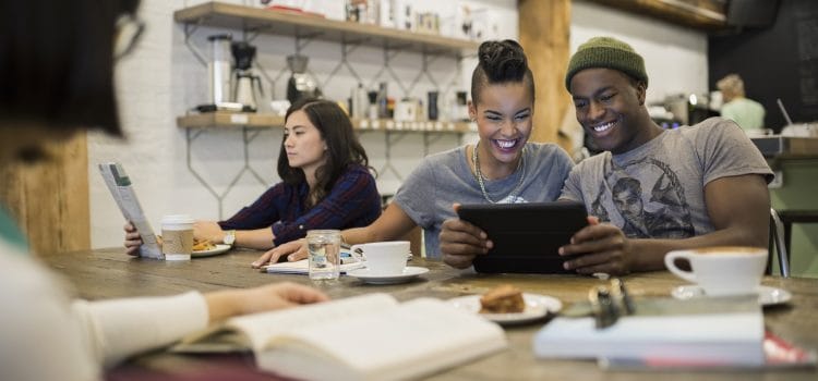 A group of people in an office breakroom. One reads and two look at a phone.