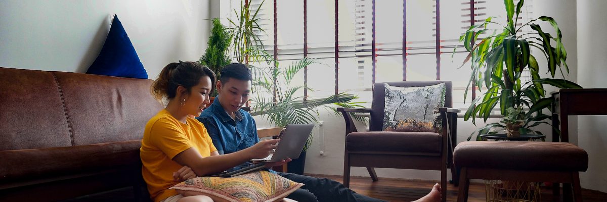 A man and a woman sit in the living room, reviewing their accounts on laptop computer.