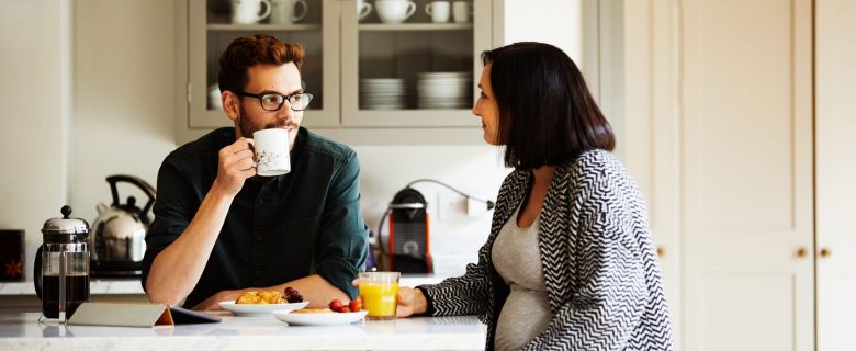A man and woman talk in the kitchen.