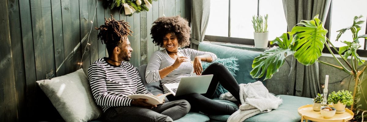 Man and woman talking about something on the couch with a laptop open.