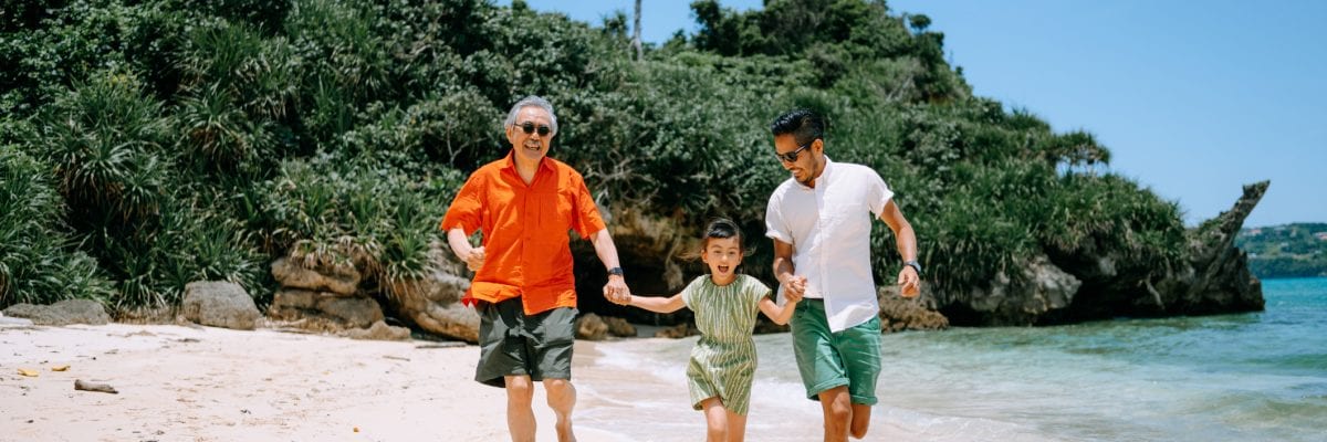 A family runs hand-in-hand along a beach on a sunny day.