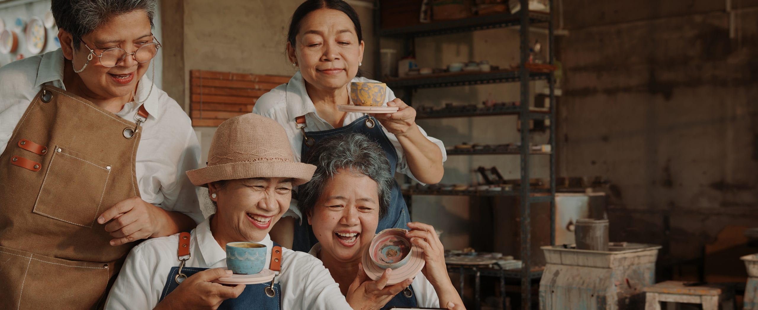A group of retired women proudly show off their handmade pottery in a studio. 